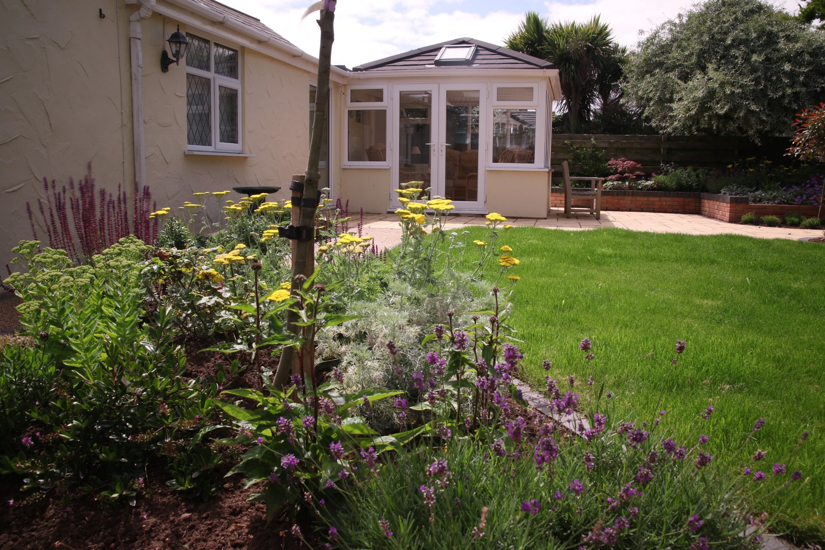 Purple and yellow flowers in decorative flower bed overlooked by a conservatory